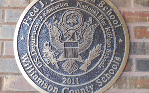  Metallic, circular crest mounted against a brick wall.
